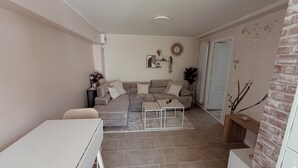 Een woonkamer met een bank, een salontafel, een bijzettafeltje met een lamp en een open haard.