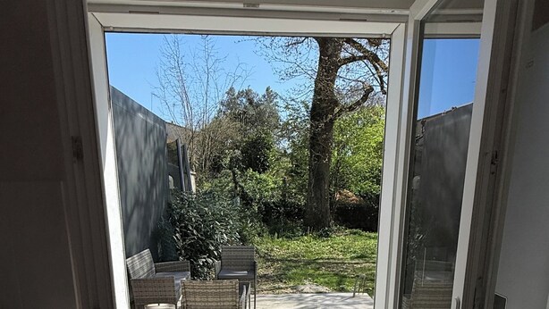 Een kamer met een schuifdeur naar een terras buiten, met een bank en stoelen.