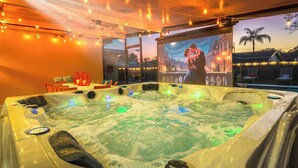 Un bain à remous avec vue sur le paysage urbain au crépuscule, entouré de guirlandes lumineuses et agrémenté d’un coin salon confortable.