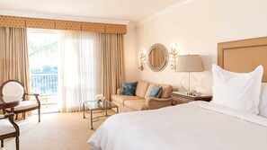 Ein Hotelzimmer mit Bett, einer Couch, einem Sessel, einem Tisch und einem Balkon mit Vorhängen.
