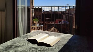 A bed with an open book, a window with curtains, and a view of buildings and a plant outside. - Cozy and spacious apartment in the heart of the historic center of Catania (Catania)