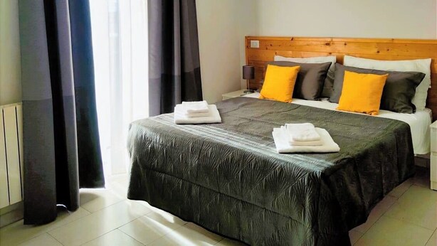 A hotel room with a large bed, dark curtains, a wooden headboard, and a yellow pendant light. - Cozy and spacious apartment in the heart of the historic center of Catania (Catania)