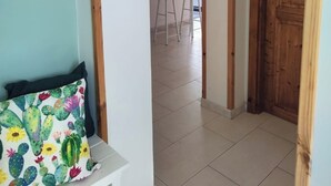 A hallway with a wooden door, a white bench with a cactus-patterned pillow, and a glimpse of a kitchen area in the background. - Cozy and spacious apartment in the heart of the historic center of Catania (Catania)