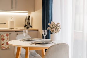 Een eettafel gedekt met borden, bestek en wijnglazen, een vaas met bloemen, en een keuken met kasten en een waterkoker.