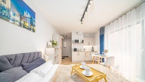 Ein modernes Wohnzimmer mit einem grauen Sofa, einem Holztisch mit Tassen, einer Küche im Hintergrund und einem Stadtbild an der Wand.