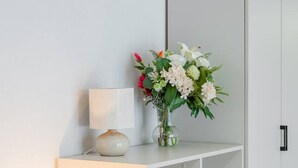 Ein weißes Schränkchen mit einer Blumenvase und einer Lampe darauf.
