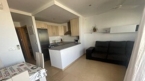 Et moderne køkken med en central ø, et spisebord med stole, en sort sofa og en lille plante på en hylde.