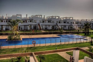 A modern hotel with a central swimming pool, surrounded by a fenced area and a well-maintained lawn. - Condado De Alhama Apt-pool-park-parking-sleeps4 (Alhama de Murcia)