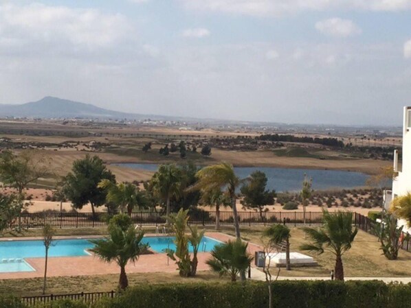 Área de piscina com palmeiras e vista para uma paisagem distante, incluindo um corpo d'água e montanhas.