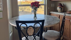 A dining area with a round table, two chairs, and a vase with red flowers.