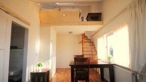 Ein kompakter Wohnraum mit Schlafgalerie, einer Essecke mit Holztisch und -stühlen sowie einer Treppe zum oberen Bereich.
