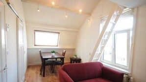 Ein Zimmer mit Esstisch, Stühlen, einem roten Sofa, einem Fenster mit Aussicht und Holzboden.
