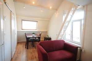 Una habitación con una mesa de comedor, sillas, un sofá rojo, un ventanal y suelo de madera.