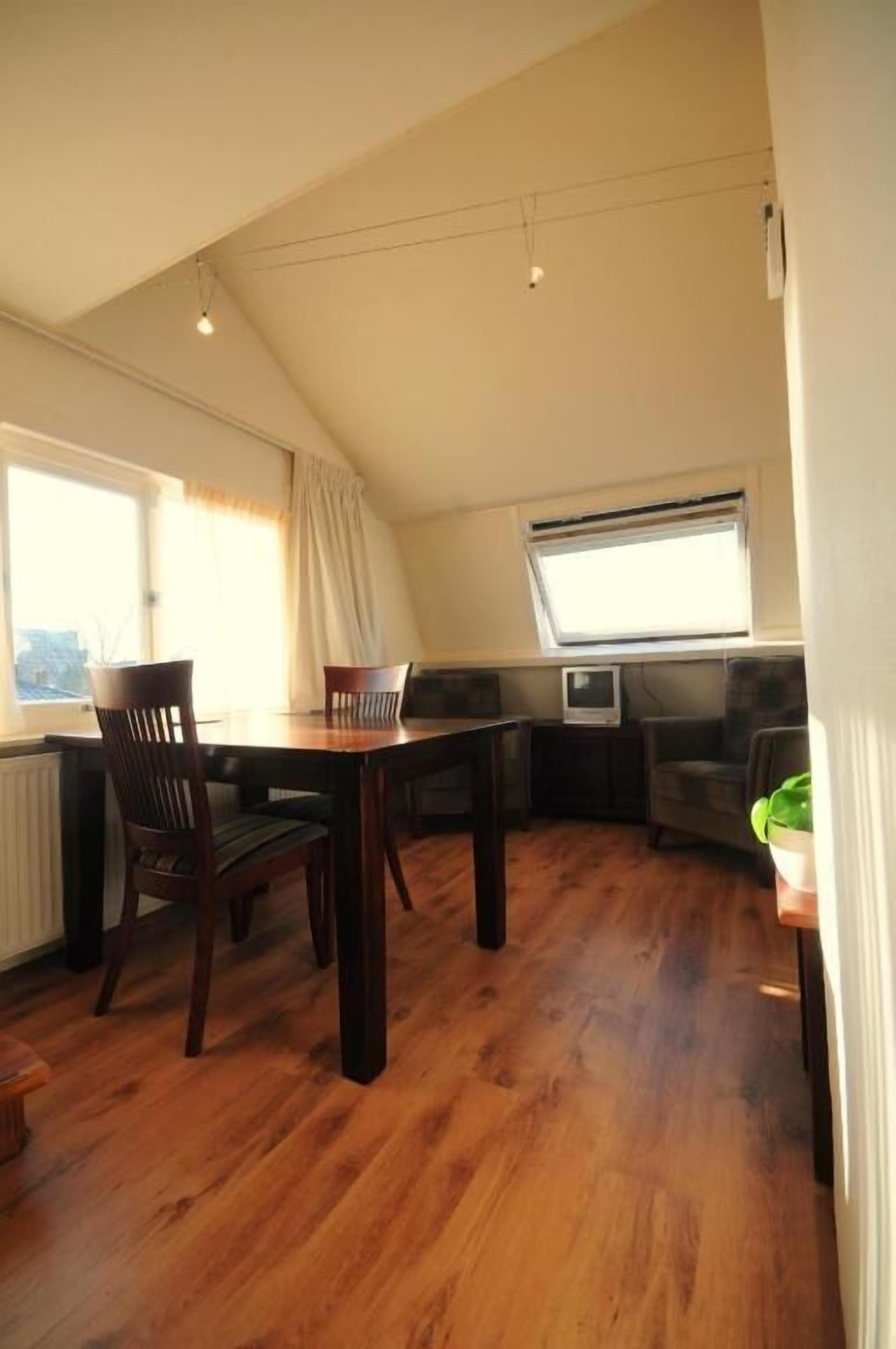 A dining area with a wooden table and chairs, a television, and a window with curtains.