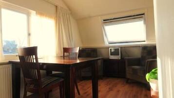 A dining area with a wooden table and chairs, a television, and a window with curtains.