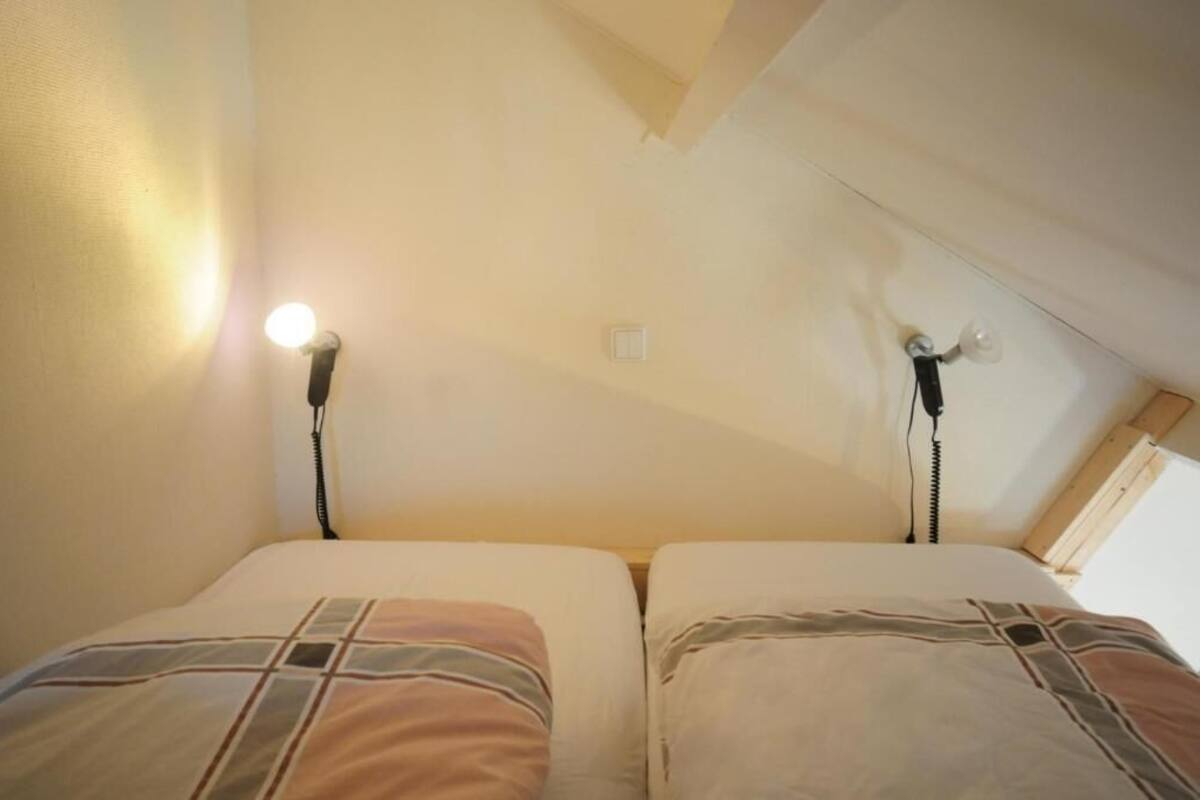 A small, cozy room with two beds, each with a patterned bedspread. There are two bedside lamps and a ceiling light.
