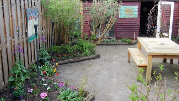 Ein Garten mit Holztisch und Bänken, einem Holzzaun und einem kleinen Schuppen.