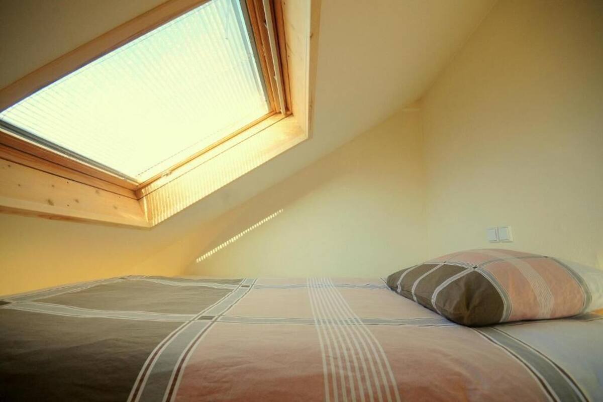 A bedroom with a skylight, a bed with striped bedding, and a wall socket.
