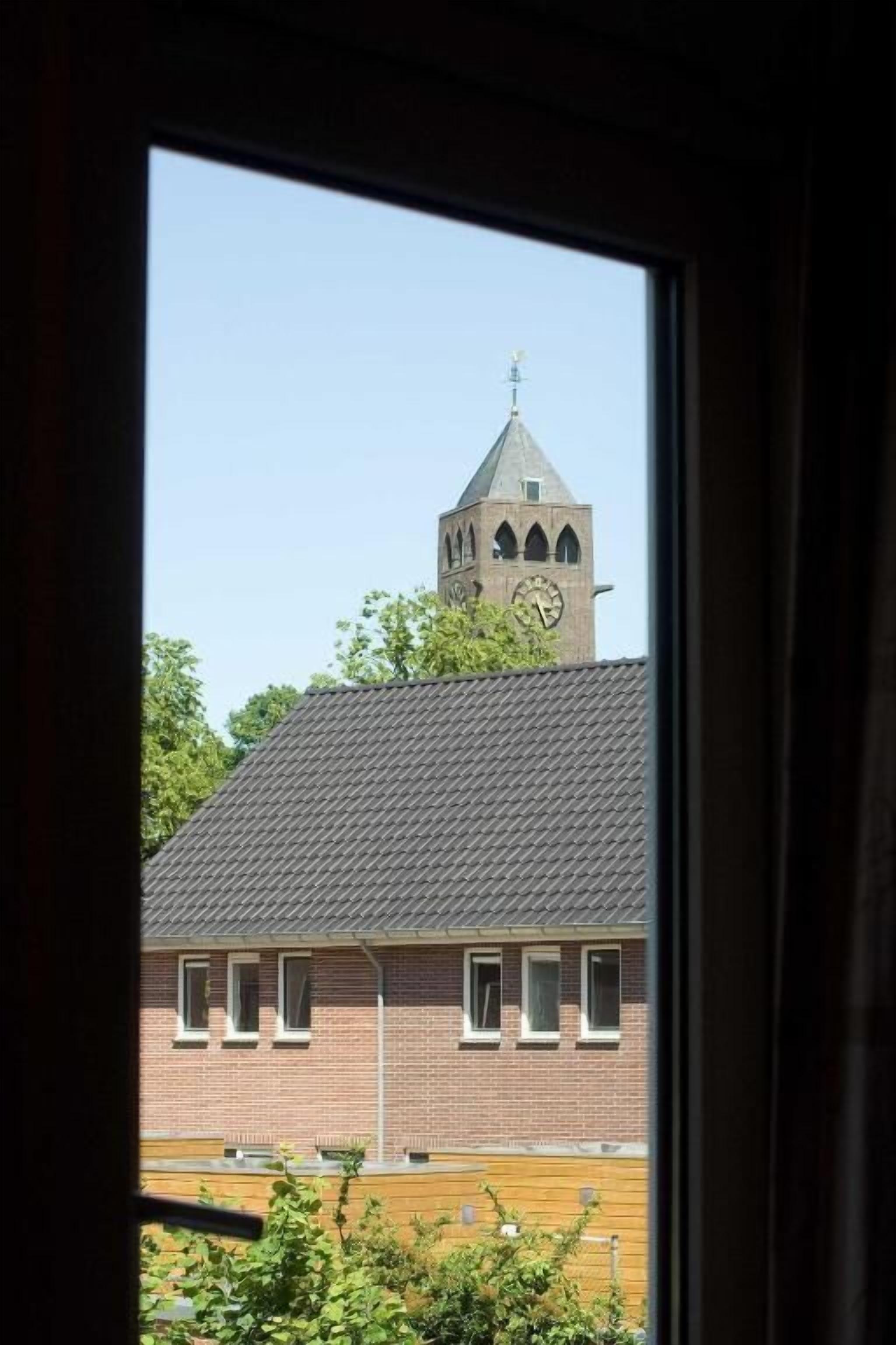 Vista per una finestra d'un edifici amb una torre de l'ajuntament, façana de rajol i cel blau.