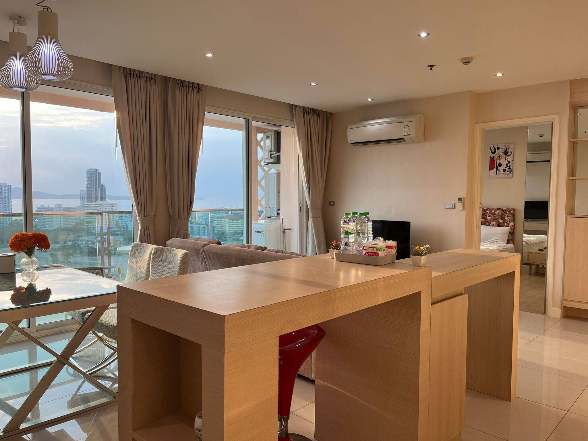 Een moderne woonkamer met een glazen eettafel, een bank, een rode fauteuil en een keuken met een televisie en een koelkast.