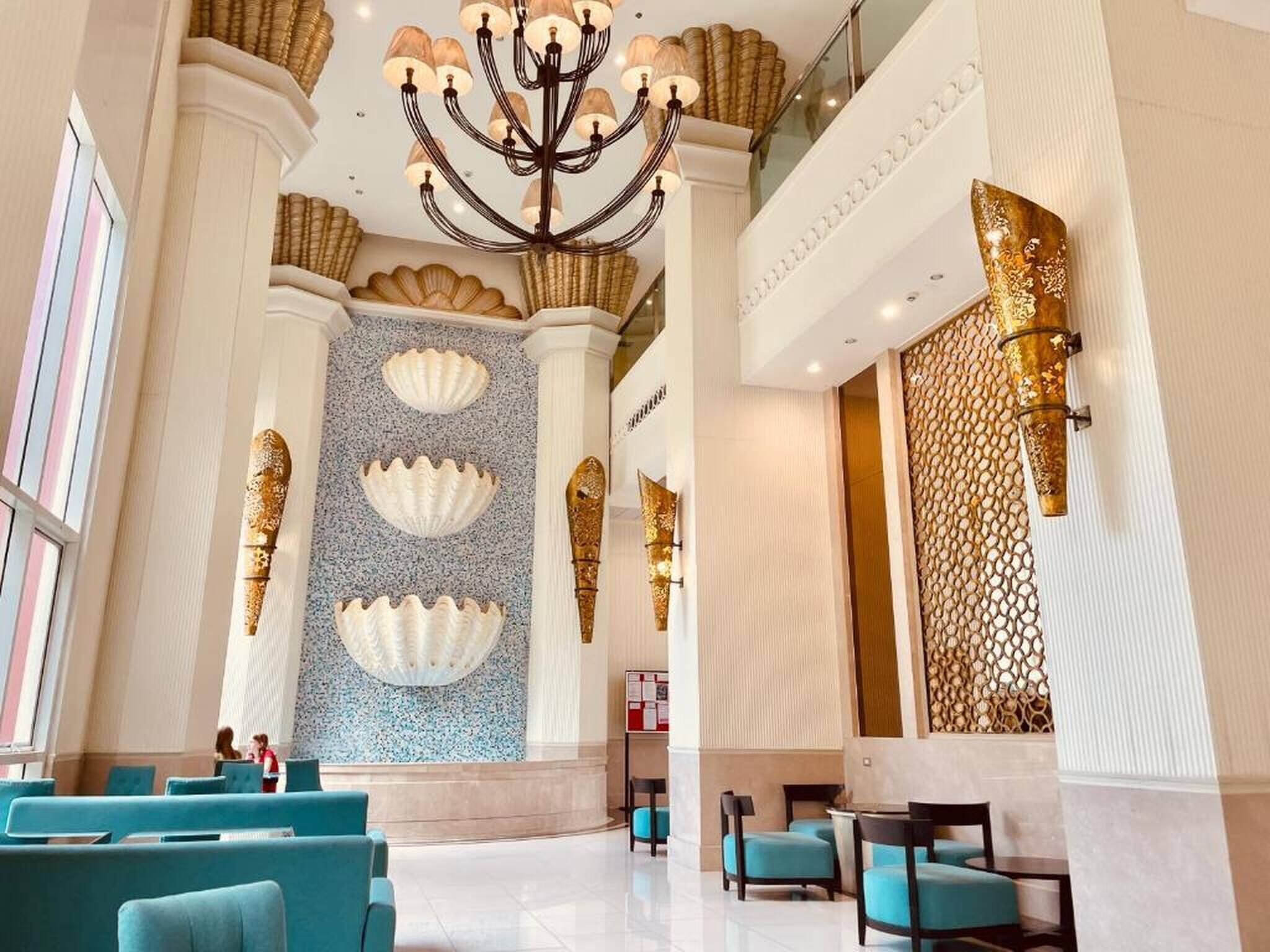 Un hall d’entrée spacieux agrémenté d’un lustre, de coins salon et de panneaux muraux décoratifs.