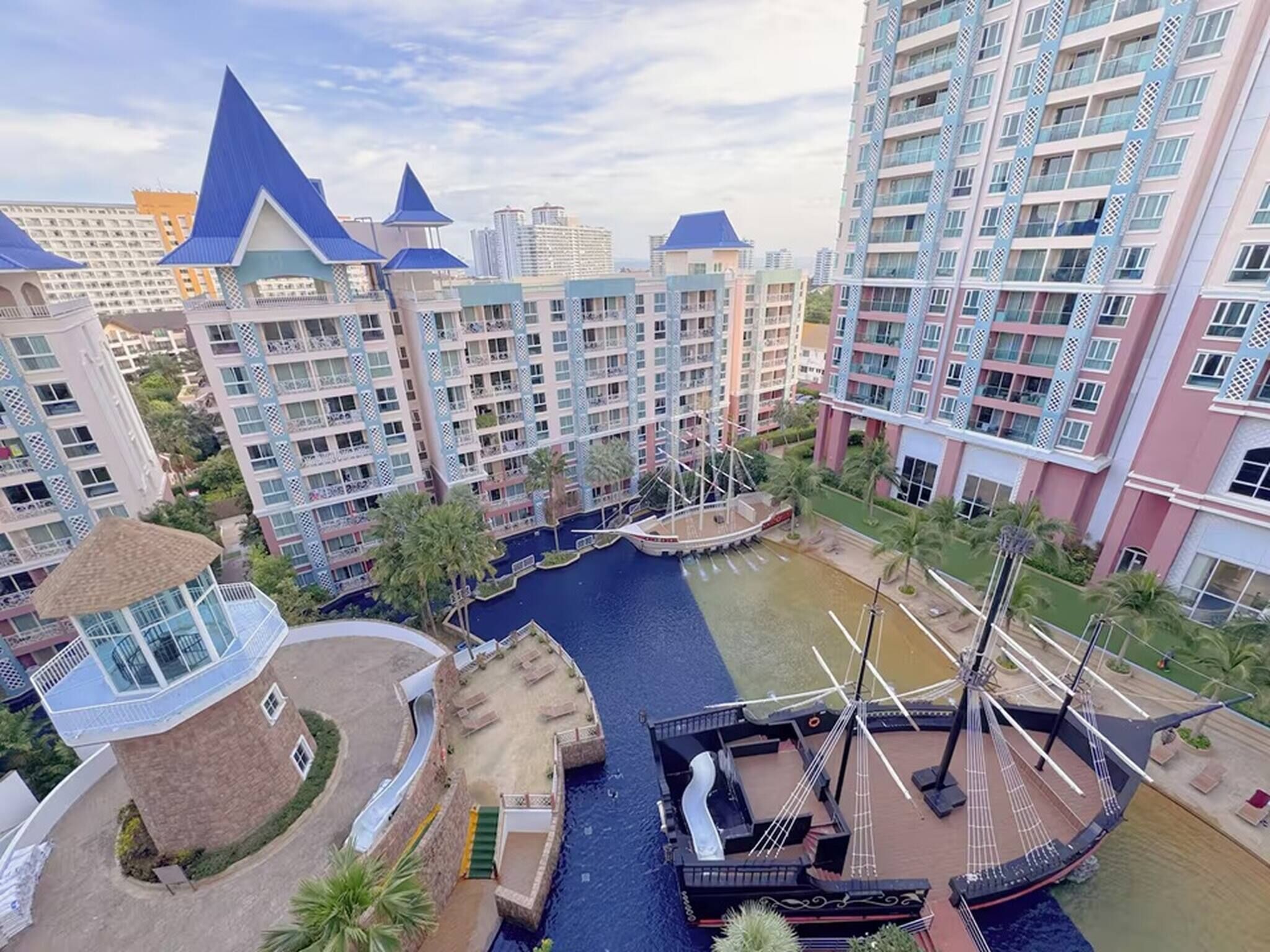 A high-rise hotel with multiple balconies, a central courtyard with a water feature, and a small boat dock.