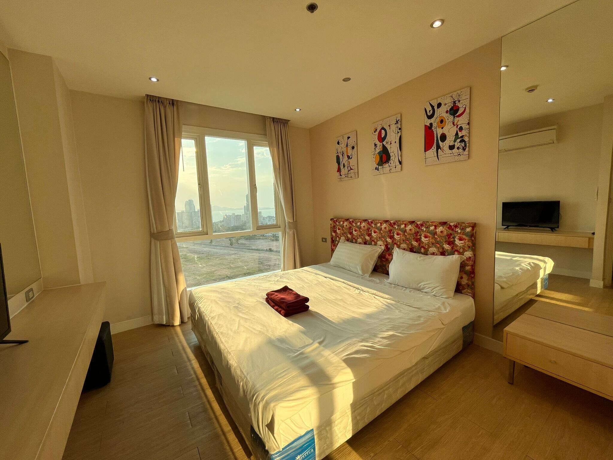 A hotel room with a large bed, a TV, a desk, and a window with a city view.
