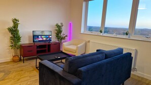 Uma sala de estar moderna com televisão, sofá, poltrona e plantas em vasos.