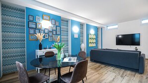A modern living room with a blue accent wall, a dining area with a glass table, and a flat-screen TV mounted on the wall. - Italianway Easy - Andrea del Sarto 32 (Milan)