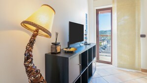 Ein modernes Interieur mit einem Fernseher auf einer dunklen Konsole, einer Zierleuchte und Blick durch eine Tür.