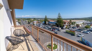 Ein Balkon mit zwei Stühlen und Blick auf einen Parkplatz sowie eine Straße mit Gebäuden und Bäumen in der Ferne.