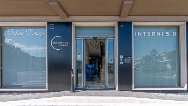 Ein Gebäude mit großen Fenstern, einer Beschilderung mit 'Italian Design' und einer Tür, auf der 'INTERNI 5.0' steht.