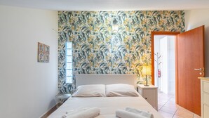Ein Hotelzimmer mit Bett, Nachttisch, Lampe, Holztür und gemustertem Wandpapier.
