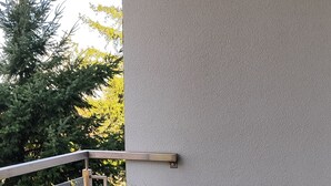 Ein Balkon mit Glasgeländer, zwei graue Stühle, ein Topfpflanze und ein kleiner Tisch.