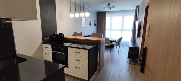 Una cocina moderna con encimera negra, armarios blancos y un comedor con mesa y sillas de madera.
