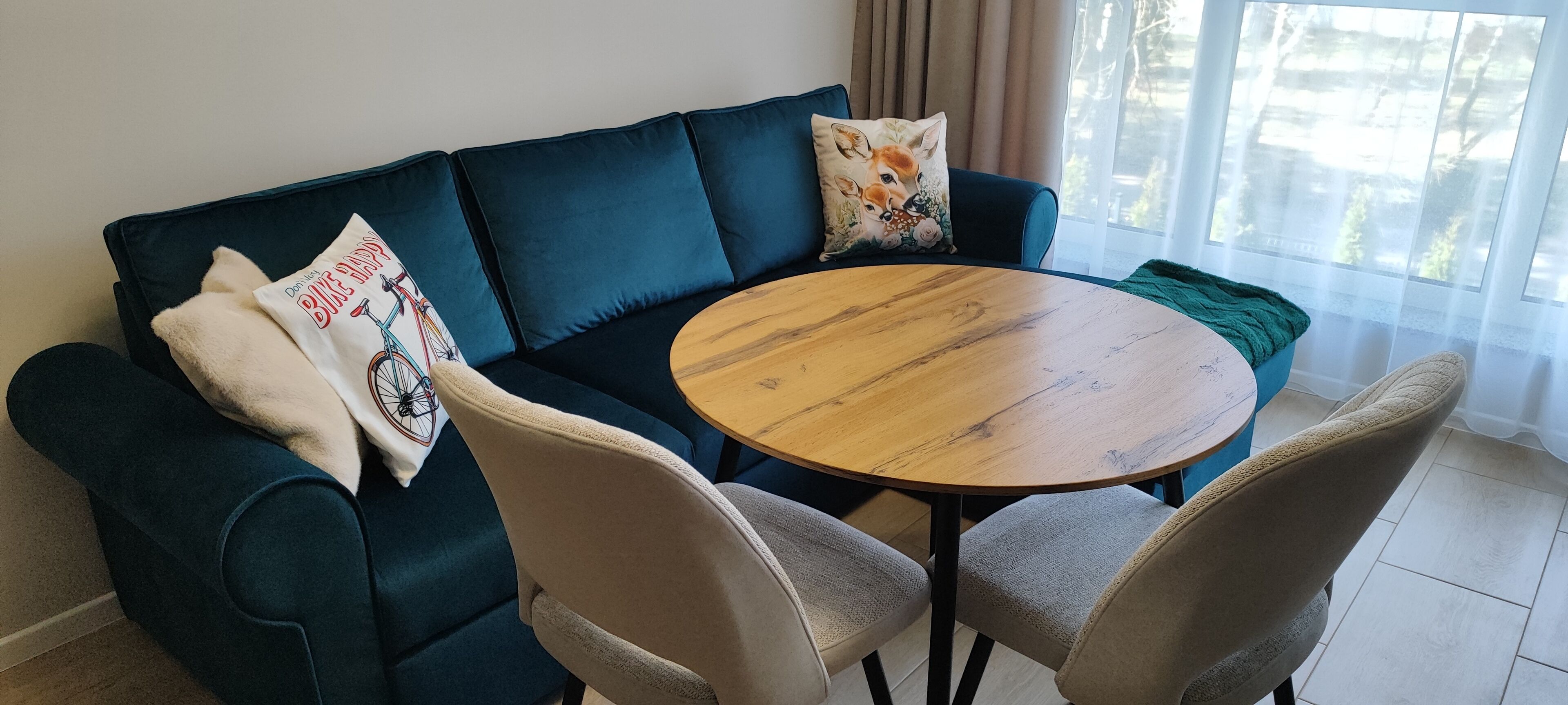 A dark blue sofa with two cushions, a round wooden table, and two beige chairs in a room with a large window.