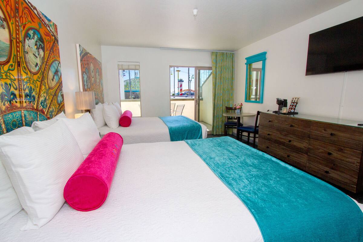A hotel room with two beds, a wooden dresser, a TV, and a balcony with a view of a building.