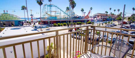A balcony with a table and chairs, overlooking a parking lot and amusement park structures.