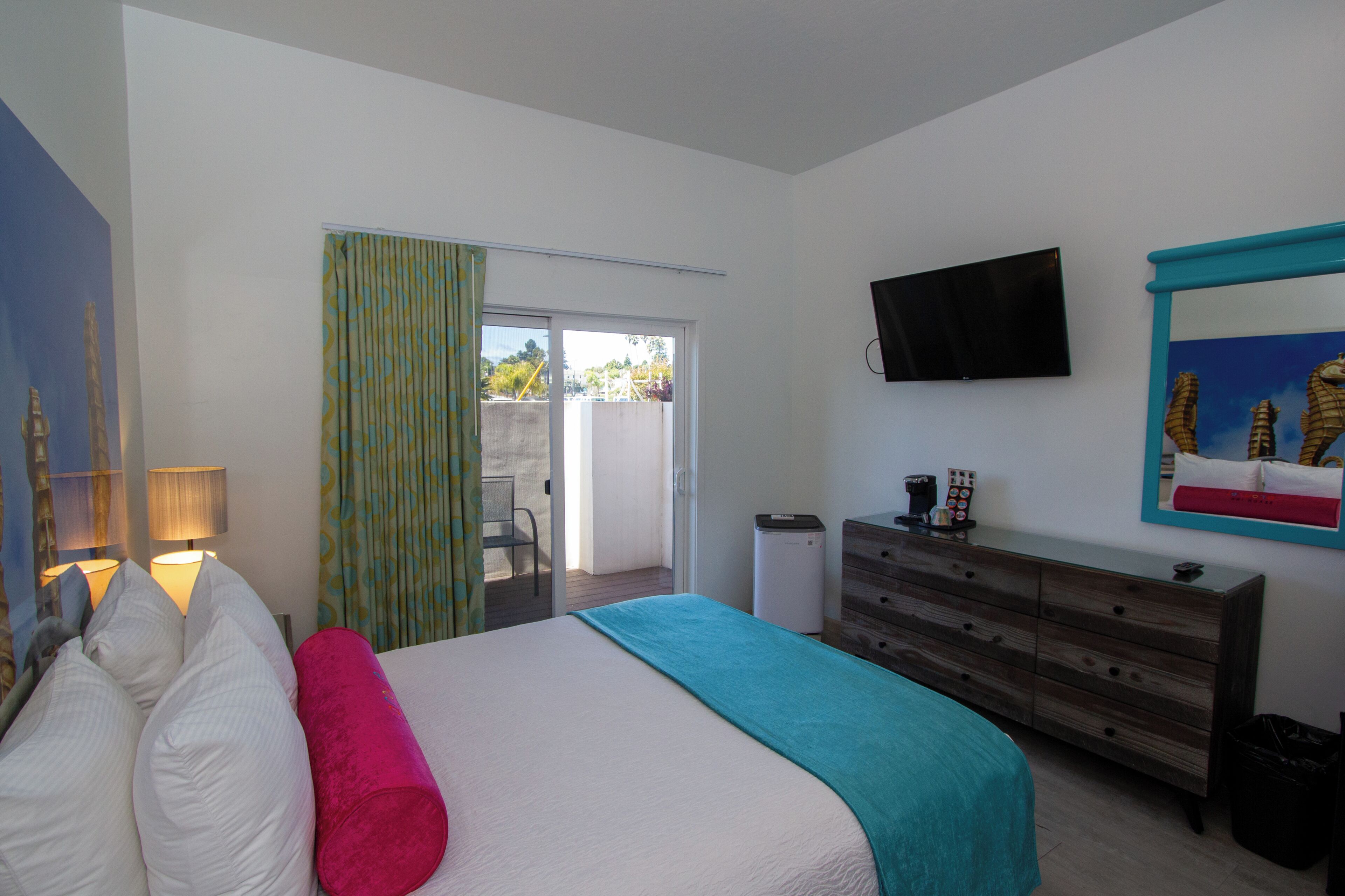 A bedroom with a bed, a dresser, a television, and a sliding glass door leading to an outdoor area.