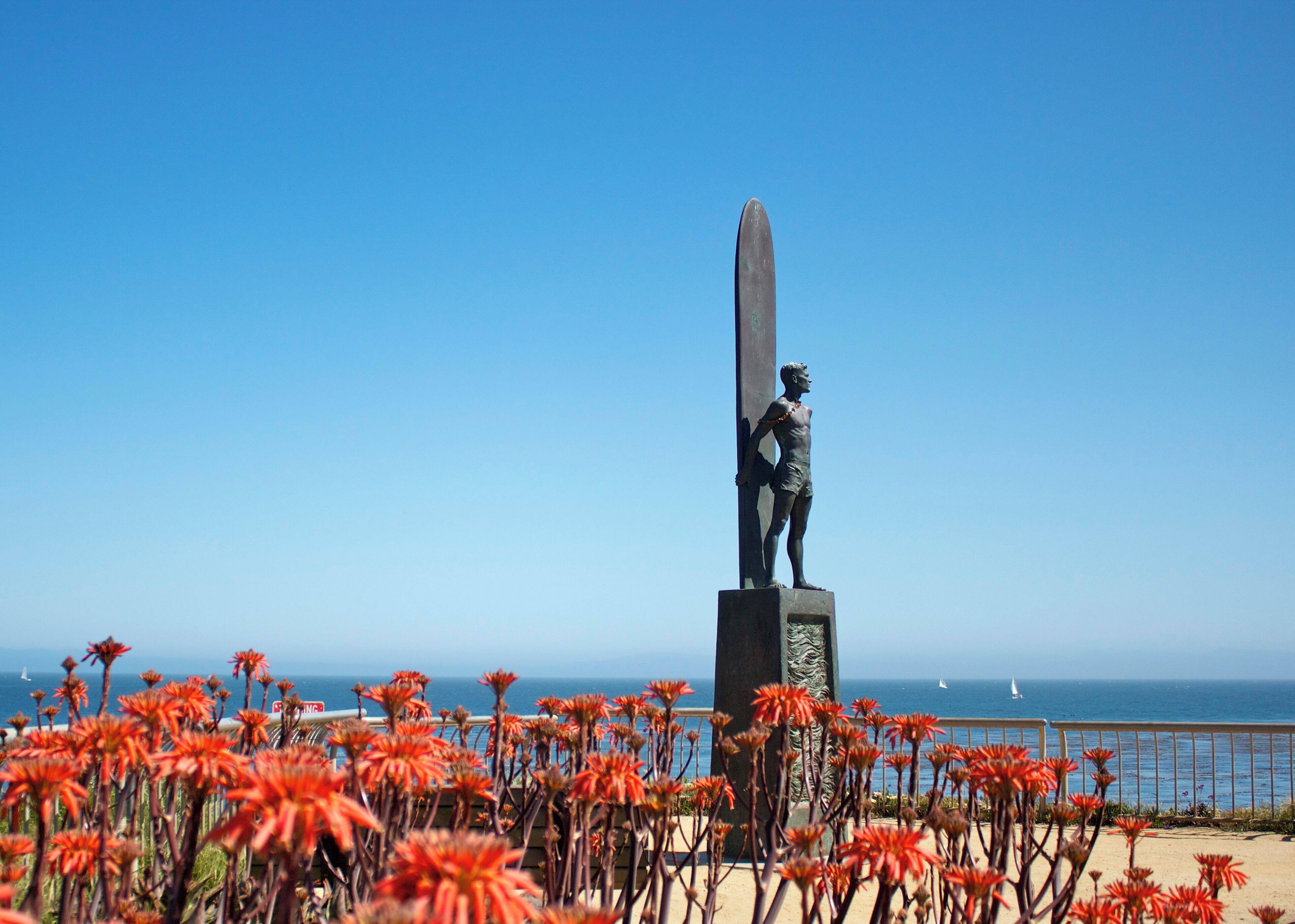A statue on a pedestal by the sea with a clear sky.