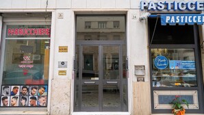 A storefront with a glass door and two visible signs, one for a barber shop and another for a pastry shop. - Naif (Rome)