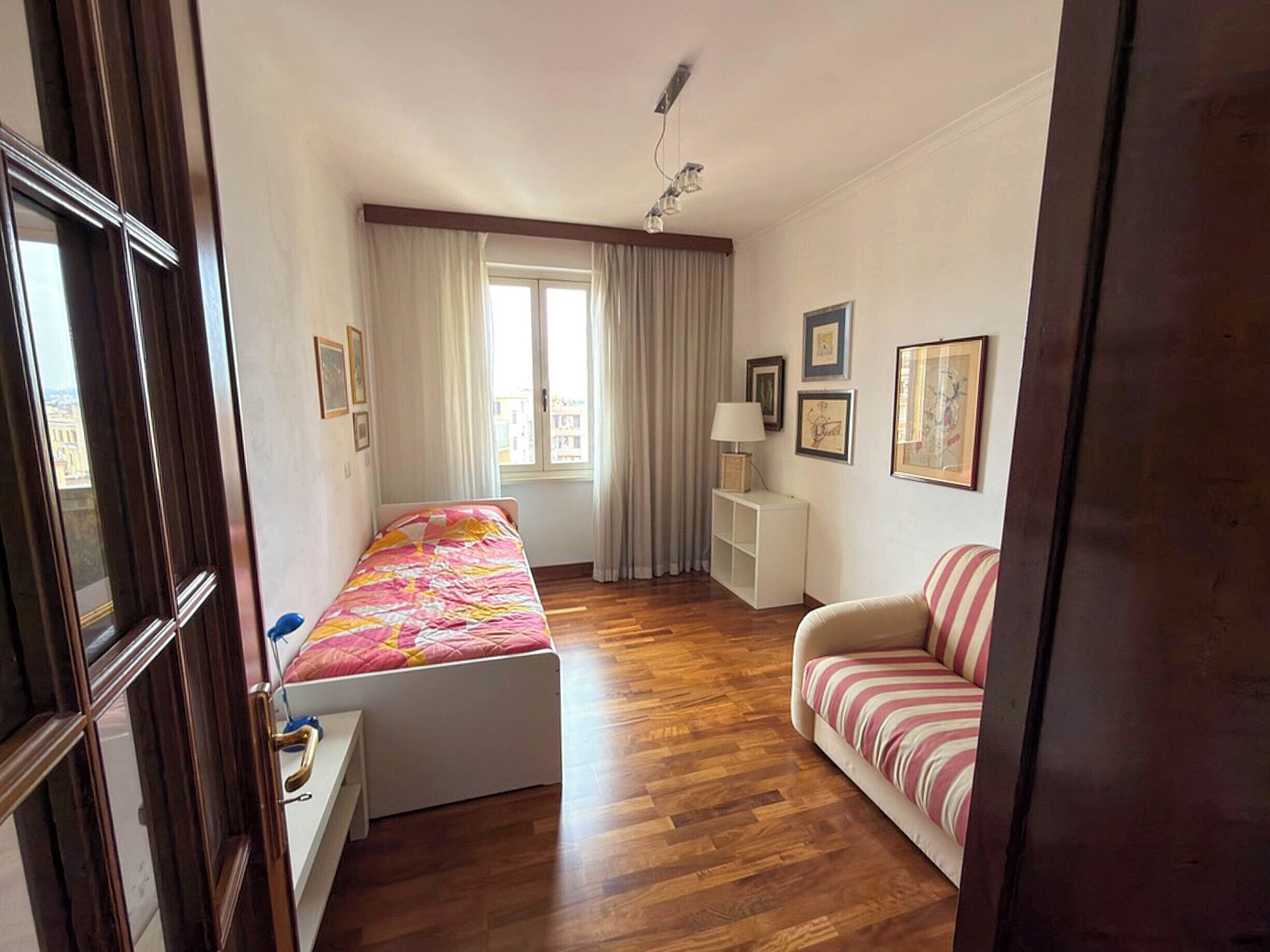 A bedroom with a bed, a desk, a chair, and a window with curtains.