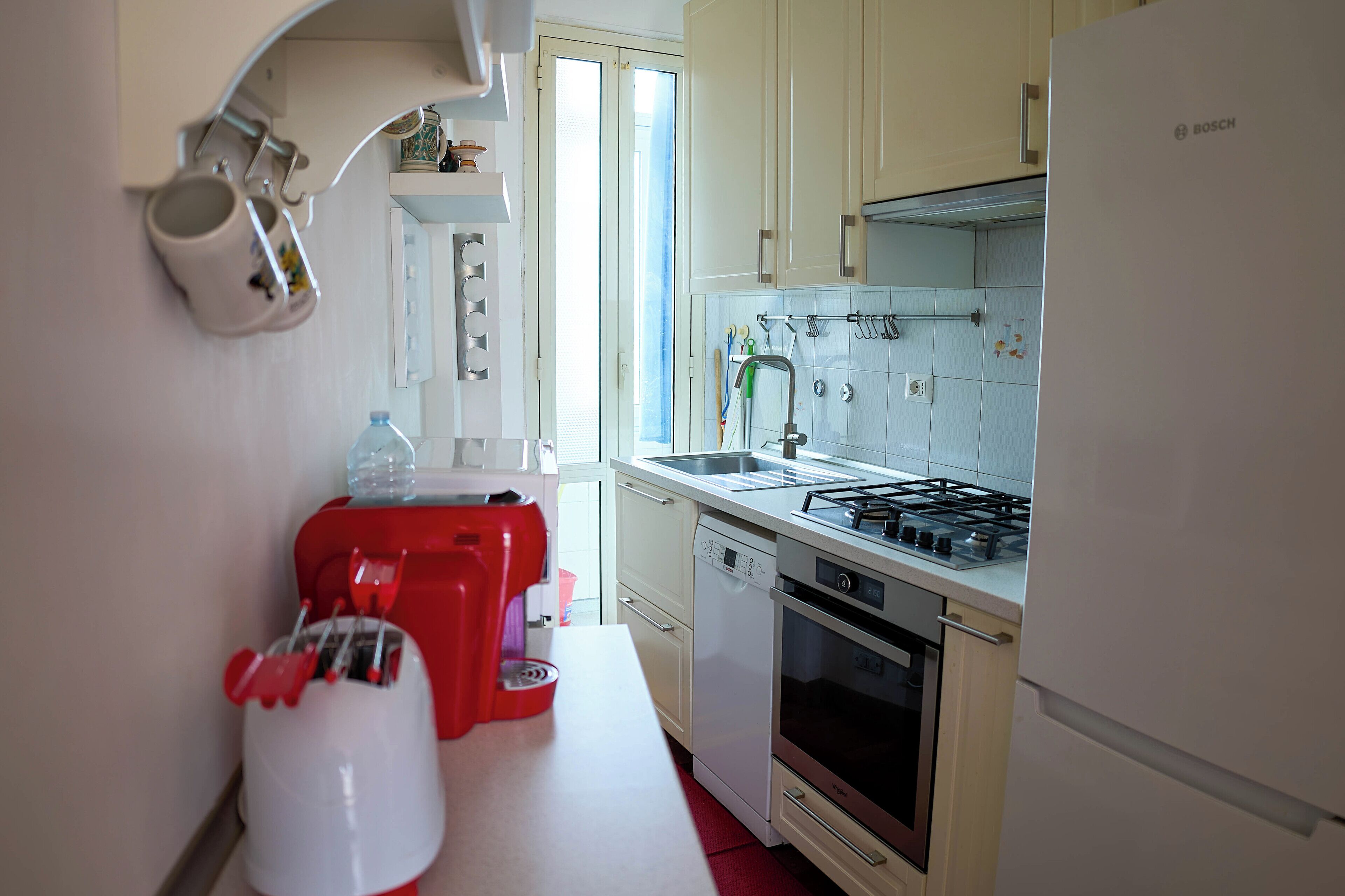 Una cocina con un refrigerador Bosch, un tostador rojo, un lavavajillas y una estufa a gas.