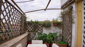 A small outdoor patio with a table and chairs, surrounded by potted plants and a lattice fence. - Naif (Rome)