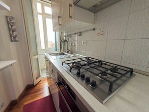Cozinha moderna com fogão de aço inoxidável, armários brancos e janela que permite entrada de luz natural.