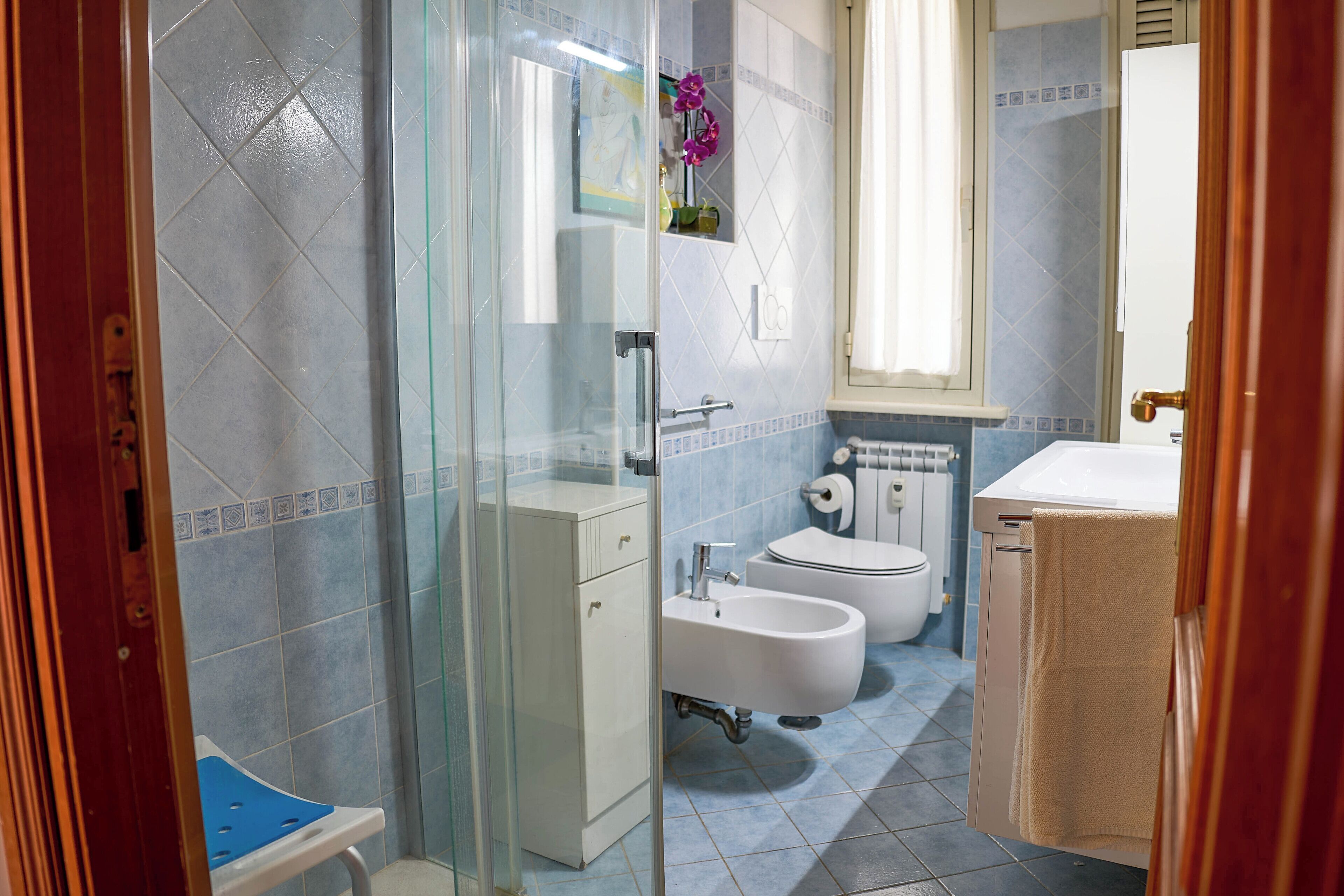 A bathroom with a glass shower enclosure, a white sink, a bidet, and a toilet.