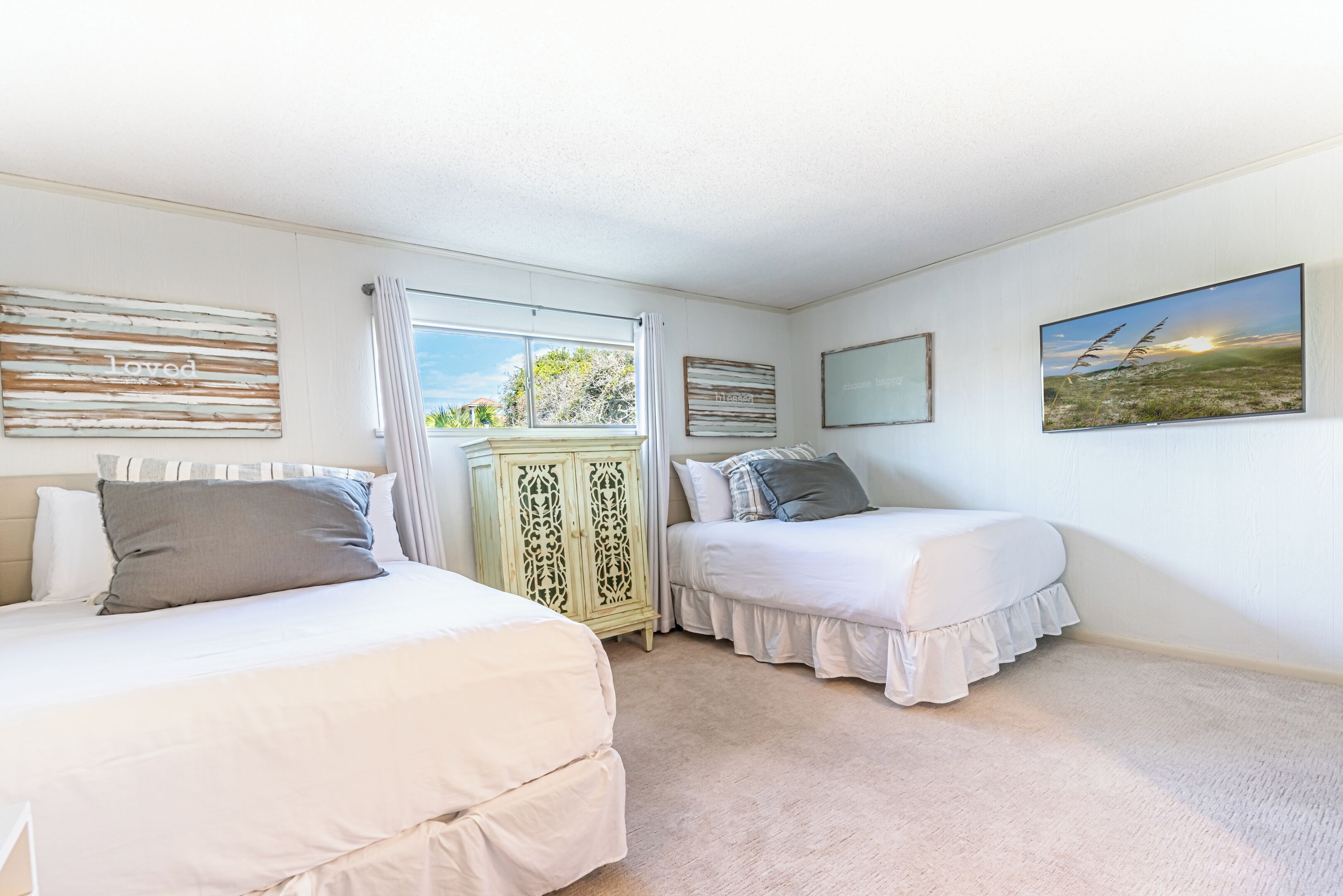 A bedroom with two beds, a window with curtains, a decorative cabinet, and wall art.