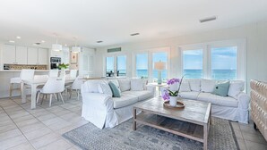 En moderne stue med en stor hvid hjørnesofa, et sofabord og et spiseområde med hvide stole og et bord.