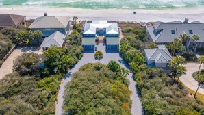 Oversigtsbillede af en ejendom ved kysten med en central bygning omgivet af frodig vegetation, beliggende ved en sandstrand.