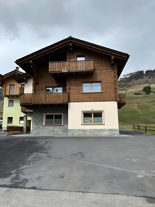 Ein mehrstöckiges Holzgebäude mit Balkonen, einem Steinsockel und Blick auf eine hügelige Landschaft.